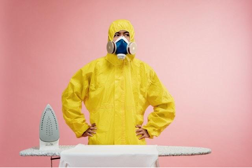 a man in yellow PVC safety suit next to an ironing board and iron